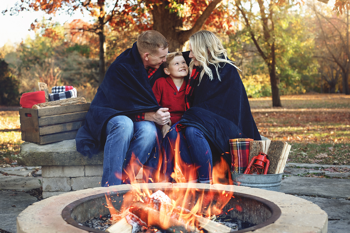 Mother, father and son wrapped in a blanket around a campfire during a family photography session in Bloomington-Normal