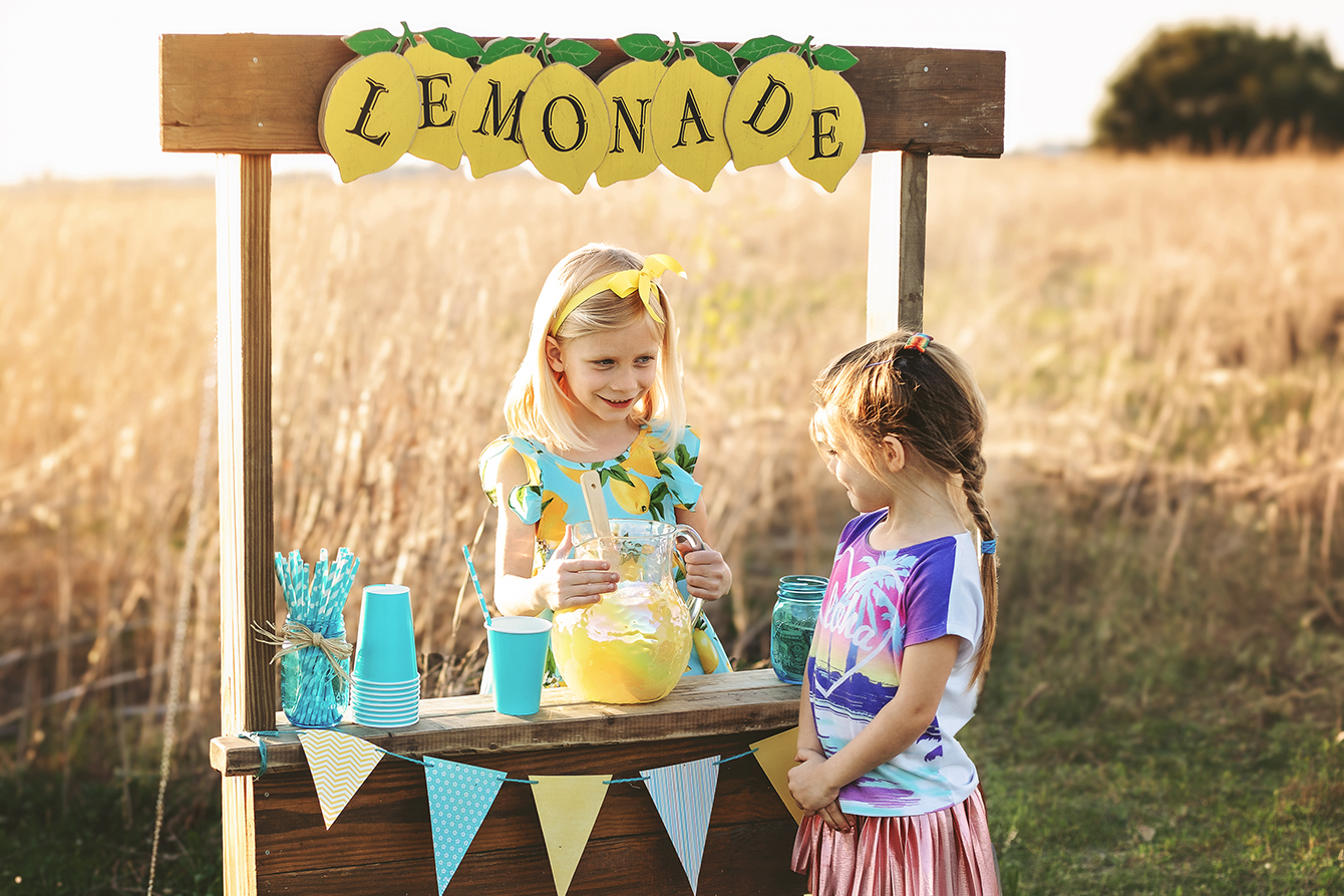 Two little girls at a stand selling lemonade